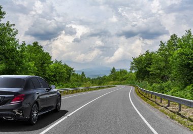 Araba, güneşli bir yaz gününde bir dağ yolunda hareket eder..