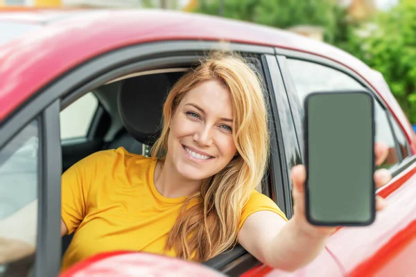 Νεαρή γυναίκα που οδηγεί αυτοκίνητο δείχνει μια οθόνη smartphone. — Φωτογραφία Αρχείου