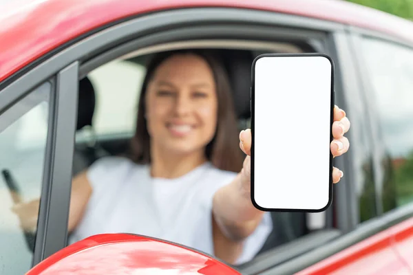 車を運転している若い女性はスマートフォンの画面を示しています. — ストック写真