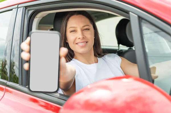 車を運転している若い女性はスマートフォンの画面を示しています. — ストック写真