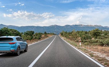 Manzaralı bir yolda mavi bir araba.