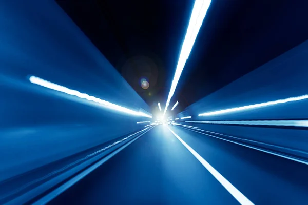 Cars rush through the tunnel in the beams of searchlights.