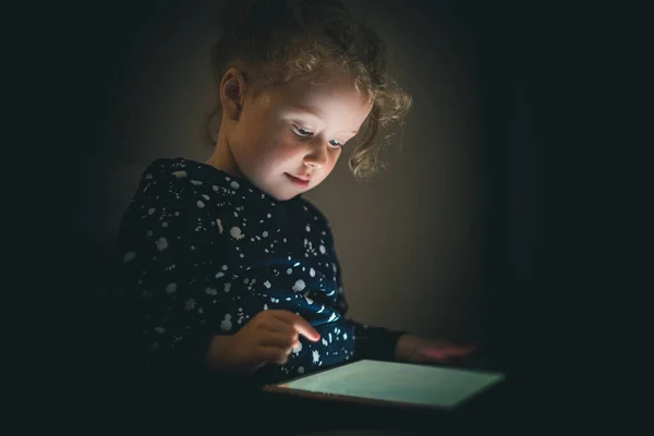Child girl with tablet in a dark room. — Stock Photo, Image