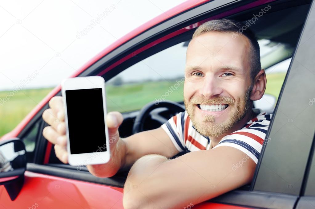 Man in car showing smart phone.