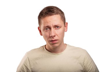 Portrait of a young man with a tired and sad expression, standing against a white background in a studio setting.