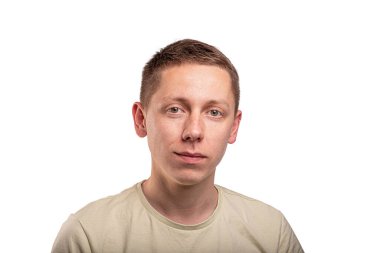 Portrait of a young man with short brown hair wearing a beige t-shirt, looking at the camera against a white studio background.