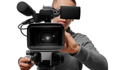 A professional cameraman operating a video camera on a tripod, focusing through the viewfinder against a white background.