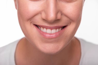 Gülümseyen bir kadının görüntüsü beyaz dişlerini ve doğal dudaklarını gösteriyor, mutluluğu, güveni ve diş sağlığını temsil ediyor..