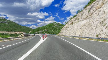 Parlak mavi bir gökyüzü altında kayalık tepelerde kıvrılan ve seyahati, özgürlüğü ve macerayı sembolize eden manzaralı dağ yolu..
