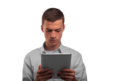 Açık renk gömlekli genç bir adam beyaz bir arkaplanda dijital tablete dikkatlice bakıyor..