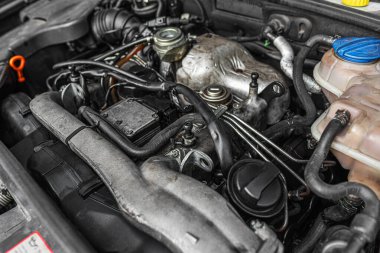 Bir otomotiv bakım veya mühendislik ayarında ayrıntılı mekanik bileşenleri, kabloları ve hortumları gösteren bir araba motoru kompartımanının yakın görüntüsü.