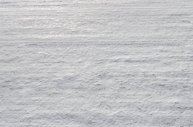 Kalıplı, karla kaplı bir yüzey parlak doğal ışık altında rüzgarın veya ışığın oluşturduğu ince sürüklenme ve yatay çizgileri gösteriyor..