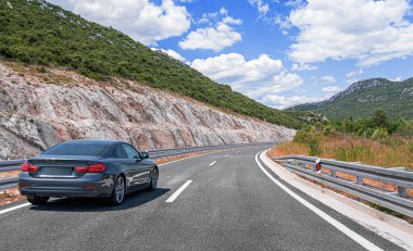 Parlak güneşli gökyüzünün altında dolambaçlı yeşil dağların arasından geçen parlak, parlak bir araba seyahat özgürlüğünü ve yaz macerasını temsil ediyor..