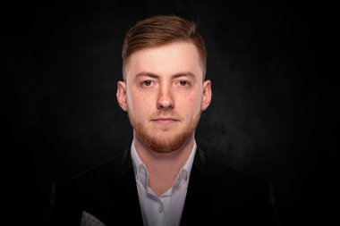 Stüdyo portresi, siyah takım elbise ve beyaz gömlekli, esmer bir arka planda sakallı, ciddi bir genç işadamının resmi..