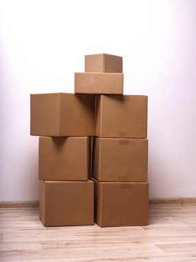 Basit bir iç mekanda düz bir duvara karşı kahverengi karton kutular dizilmiştir..