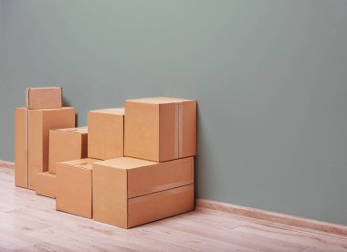 Bir yığın düz kahverengi mukavva hareket ediyor ya da depolama kutuları hafif ahşap bir zeminde nötr yeşil bir duvara karşı duruyor, bu da yer değiştirme veya depolama anlamına gelir..