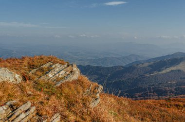 Berrak mavi bir gökyüzünün altında kayalık, çimlerle kaplı bir tepeden yuvarlanan dağların manzaralı manzarası..