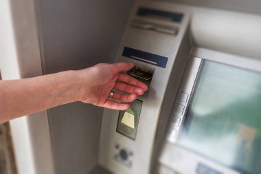 Bankacılık işlemleri yapmak için otomatik veznedar makinesine kredi kartı takan bir kişi..