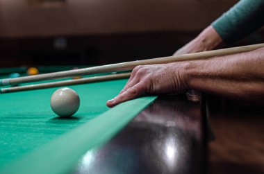 Yeşil keçeli bilardo masasındaki beyaz bilardo topunu hedef alan bir insan eli..