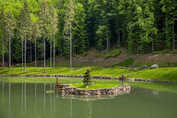 İnsan yapımı sakin bir gölette, durgun sularda yansıyan uzun çam ağaçları ile yemyeşil bir orman zeminine kurulmuş, tek bir yeşil ağacı olan küçük, taş duvarlı bir ada bulunur..