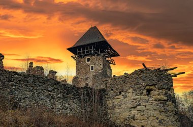 Önde gelen bir gözetleme kulesi olan taştan bir ortaçağ kalesi dramatik bir turuncu ve altın gün batımı gökyüzüne karşı duruyor. Nevitsky Kalesi, Transcarpathia, Ukrayna.