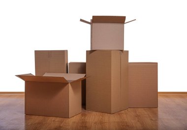 Tahta zeminde beyaz bir zemine karşı yığılmış karton kutular bir taşınma ya da taşınma konseptini ortaya koyuyor..