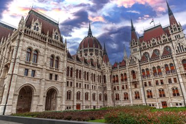 Macar Parlamento Binası dramatik ve renkli bir gökyüzünün altında karmaşık neo-gotik mimari detaylar ve merkezi bir kubbe ile duruyor..