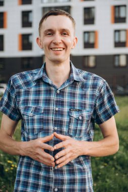 Genç bir adam, kollarını kavuşturmuş, ekose gömlekli fotoğraf çekiminde poz veriyor..