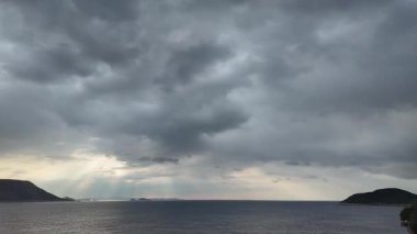 Hızla yaklaşan yağmur ufka yaklaşırken sakin denizin ve uzak adaların üzerinde toplanan kara fırtına bulutlarını gösteriyor..