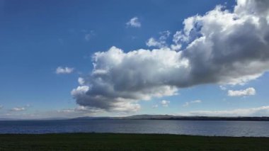 Zaman atlaması, sakin bir gölün üzerindeki açık mavi gökyüzünde yavaşça sürüklenen büyük bir kümülüs bulutunu gösteriyor. Sinematik hava görüntüleri, rahatlatıcı filmler ve doğa belgeselleri için ideal..
