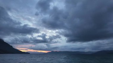 Fırtına bulutlarının ardında gün doğumu deniz ve dağların üzerinde dramatik sabah gökyüzü ve hareketli ışık