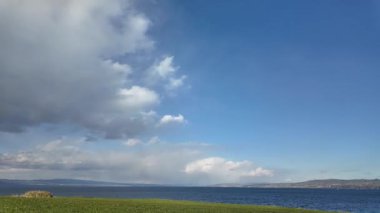 Zamanda hızla ilerleyen beyaz kümülüs bulutları sakin suyun üzerinde berrak mavi bir gökyüzünde sürükleniyor. Hava görüntüleri, sinematik doğa sahneleri ve rahatlama geçmişi için mükemmel..