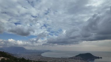 Türkiye 'nin Alanya kıyısındaki tatil beldesi üzerinde hareket eden bulutları kaydeden hızlandırılmış video. Film dinamik hava modellerini, şehir hareketlerini ve dramatik bir gökyüzünün altındaki geniş Akdeniz kıyılarını gösteriyor.