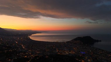 Türkiye 'nin Alanya kentinin hava panoramik manzarası, gün doğumunda hafif aydınlatılmış şehir manzarası, kıvrımlı kıyı şeridi ve sakin Akdeniz koyunu gösteriyor