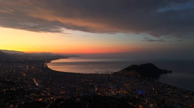 Türkiye 'nin Alanya kentinin hava panoramik manzarası, gün doğumunda hafif aydınlatılmış şehir manzarası, kıvrımlı kıyı şeridi ve sakin Akdeniz koyunu gösteriyor