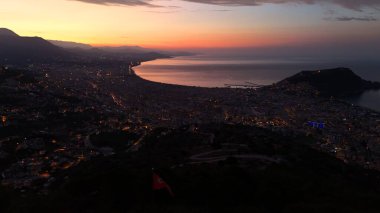 Türkiye 'nin Alanya kentinin hava panoramik manzarası, gün doğumunda hafif aydınlatılmış şehir manzarası, kıvrımlı kıyı şeridi ve sakin Akdeniz koyunu gösteriyor