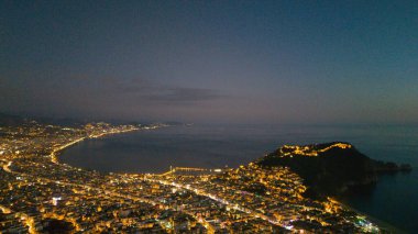 Türkiye 'nin Alanya kentinin hava panoramik manzarası, gün doğumunda hafif aydınlatılmış şehir manzarası, kıvrımlı kıyı şeridi ve sakin Akdeniz koyunu gösteriyor