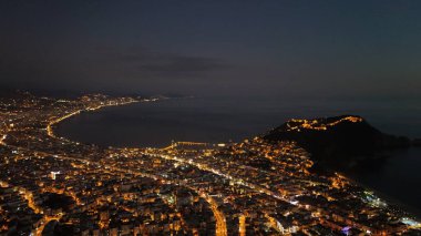 Türkiye 'nin Alanya kentinin hava panoramik manzarası, gün doğumunda hafif aydınlatılmış şehir manzarası, kıvrımlı kıyı şeridi ve sakin Akdeniz koyunu gösteriyor