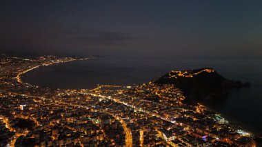 Türkiye 'nin Alanya kentinin hava panoramik manzarası, gün doğumunda hafif aydınlatılmış şehir manzarası, kıvrımlı kıyı şeridi ve sakin Akdeniz koyunu gösteriyor