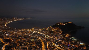 Türkiye 'nin Alanya kentinin hava panoramik manzarası, gün doğumunda hafif aydınlatılmış şehir manzarası, kıvrımlı kıyı şeridi ve sakin Akdeniz koyunu gösteriyor