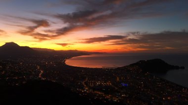 Türkiye 'nin Alanya kentinin hava panoramik manzarası, gün doğumunda hafif aydınlatılmış şehir manzarası, kıvrımlı kıyı şeridi ve sakin Akdeniz koyunu gösteriyor