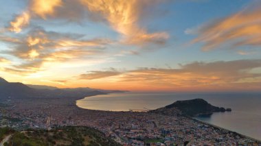 Türkiye 'nin Alanya kentinin geniş bir hava gündoğumu manzarası, şehri, körfezi ve kıyı şeridini sabahın erken saatlerinde sıcak ışıkla aydınlatıyor. Sakin deniz, uzak dağlar ve altın gökyüzü