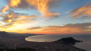 Türkiye 'nin Alanya kentinin geniş bir hava gündoğumu manzarası, şehri, körfezi ve kıyı şeridini sabahın erken saatlerinde sıcak ışıkla aydınlatıyor. Sakin deniz, uzak dağlar ve altın gökyüzü