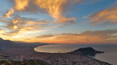 Türkiye 'nin Alanya kentinin geniş bir hava gündoğumu manzarası, şehri, körfezi ve kıyı şeridini sabahın erken saatlerinde sıcak ışıkla aydınlatıyor. Sakin deniz, uzak dağlar ve altın gökyüzü