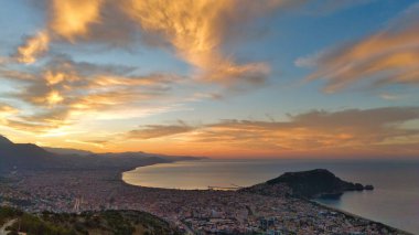 Türkiye 'nin Alanya kentinin geniş bir hava gündoğumu manzarası, şehri, körfezi ve kıyı şeridini sabahın erken saatlerinde sıcak ışıkla aydınlatıyor. Sakin deniz, uzak dağlar ve altın gökyüzü