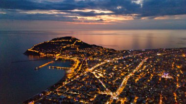 Türkiye 'nin Alanya kentinin insansız hava aracı tarafından ele geçirilmiş bir panoraması, aydınlık kenti, yarımadasını ve limanı sakin bir deniz ve alacakaranlık gökyüzüne karşı gösteriyor.