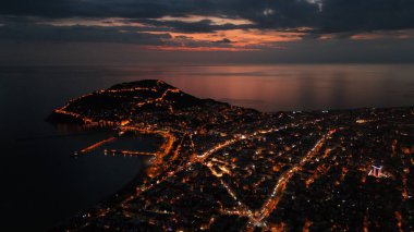 Türkiye 'nin Alanya kentinin insansız hava aracı tarafından ele geçirilmiş bir panoraması, aydınlık kenti, yarımadasını ve limanı sakin bir deniz ve alacakaranlık gökyüzüne karşı gösteriyor.