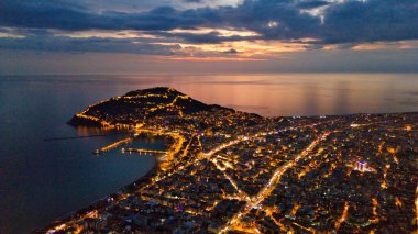 Türkiye 'nin Alanya kentinin insansız hava aracı tarafından ele geçirilmiş bir panoraması, aydınlık kenti, yarımadasını ve limanı sakin bir deniz ve alacakaranlık gökyüzüne karşı gösteriyor.