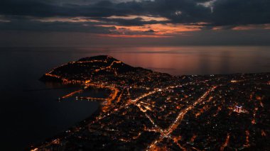 Türkiye 'nin Alanya kentinin insansız hava aracı tarafından ele geçirilmiş bir panoraması, aydınlık kenti, yarımadasını ve limanı sakin bir deniz ve alacakaranlık gökyüzüne karşı gösteriyor.