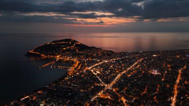 Türkiye 'nin Alanya kentinin insansız hava aracı tarafından ele geçirilmiş bir panoraması, aydınlık kenti, yarımadasını ve limanı sakin bir deniz ve alacakaranlık gökyüzüne karşı gösteriyor.